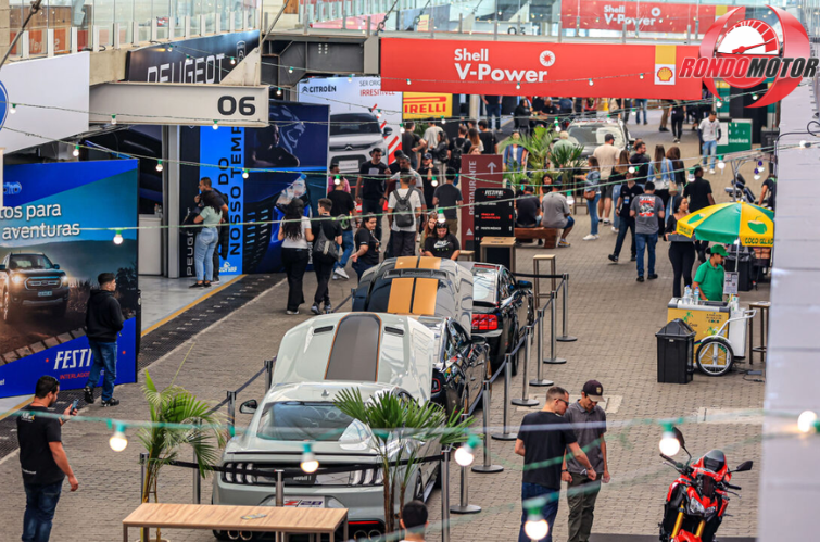Visão panorâmica do paddock, com visitantes circulando entre os carros lançados em uma plataforma multicultural montada no autódromo